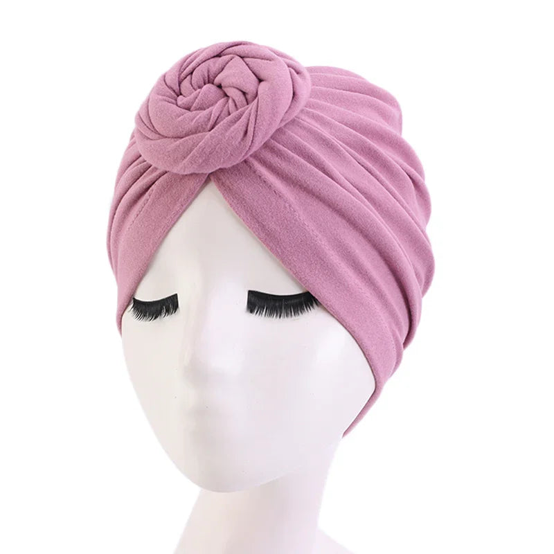 Pink fabric turban headwrap with rosette detail on white mannequin head