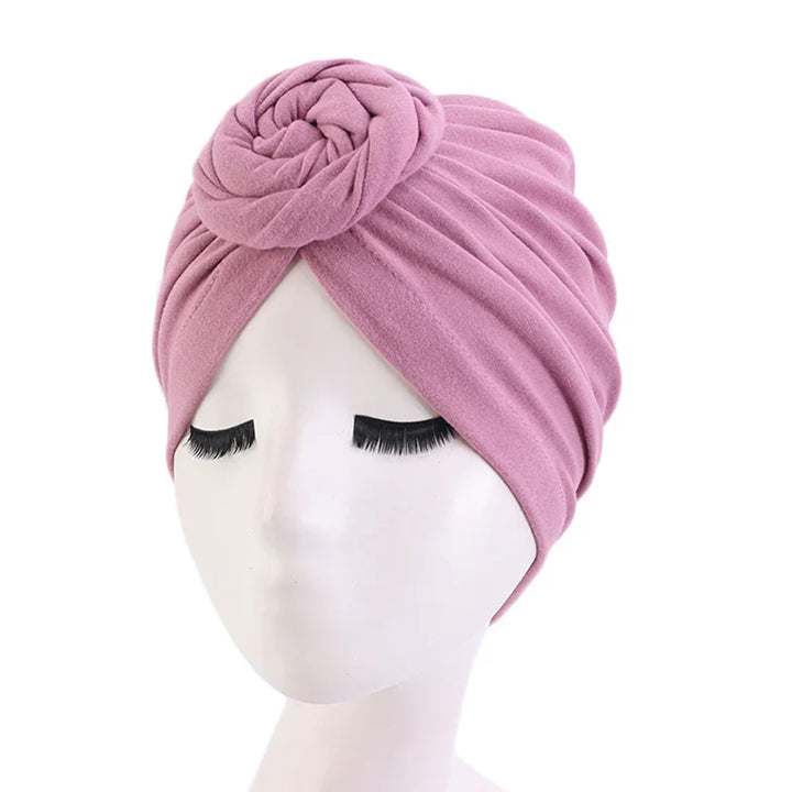 Pink fabric turban headwrap with rosette detail on white mannequin head