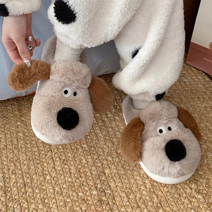 Plush dog slippers with brown ears worn with white and black polka dot fleece pants, hand adjusting slipper