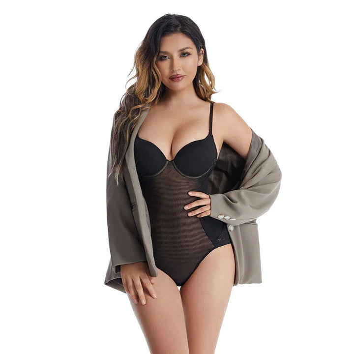 woman wearing black mesh bodysuit and gray blazer posing against white background
