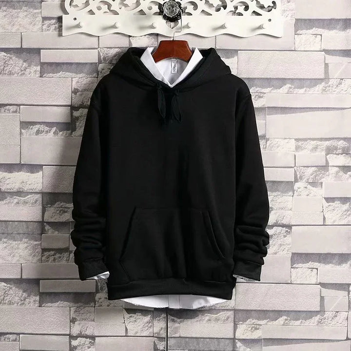 Black hoodie layered over white shirt hanging on wooden hanger against stone wall