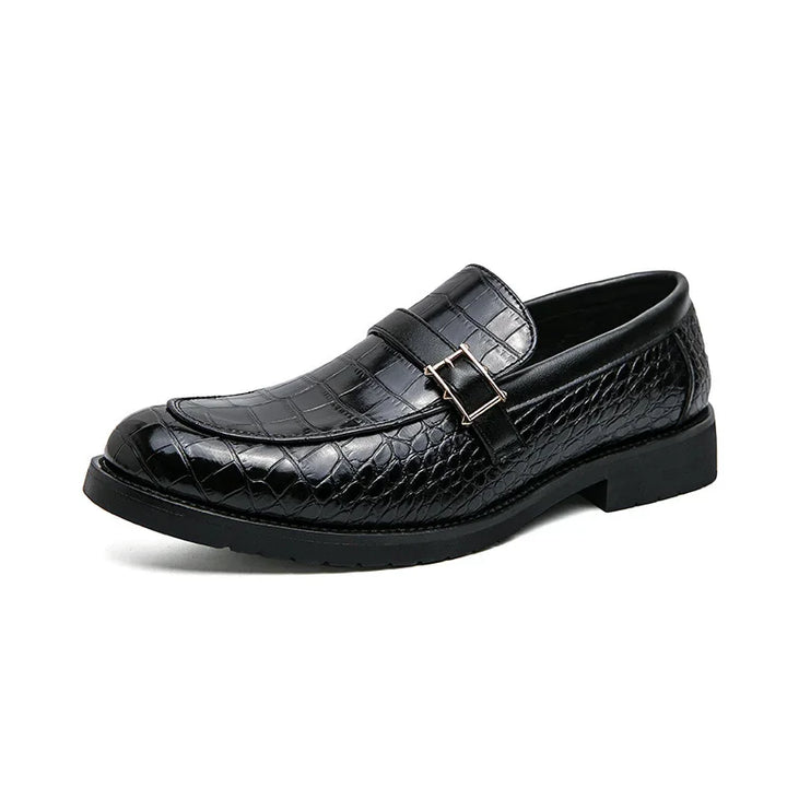 Black men's dress loafer with crocodile texture and decorative buckle on white background