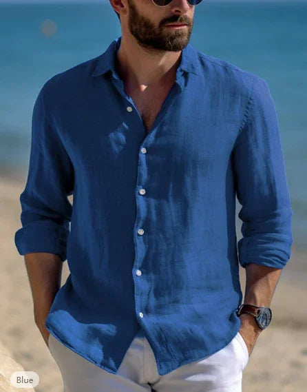 Man wearing a casual blue linen button-up shirt with rolled sleeves and white pants at the beach