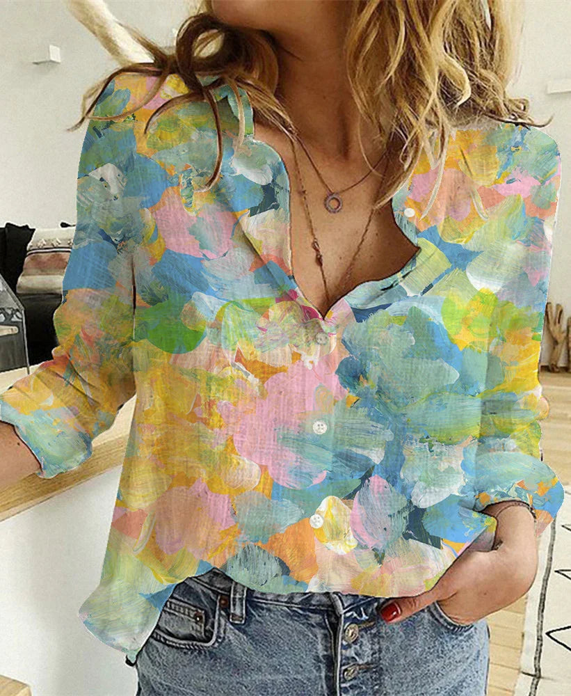 Woman wearing colorful floral print button-up blouse with rolled sleeves and denim jeans indoors
