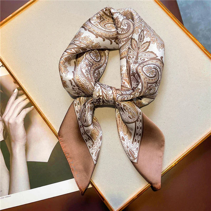 Silk scarf with beige and brown paisley pattern elegantly tied, displayed on a beige surface