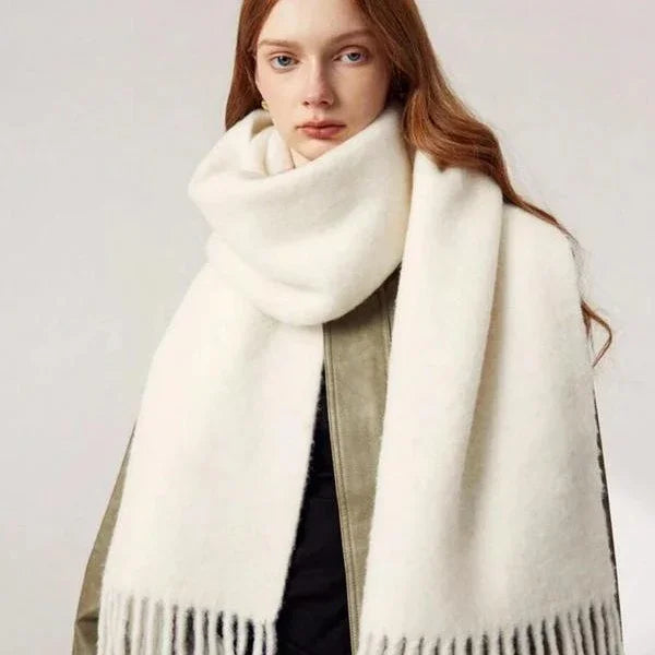 Woman wearing oversized white fringed winter scarf and olive green jacket against plain background