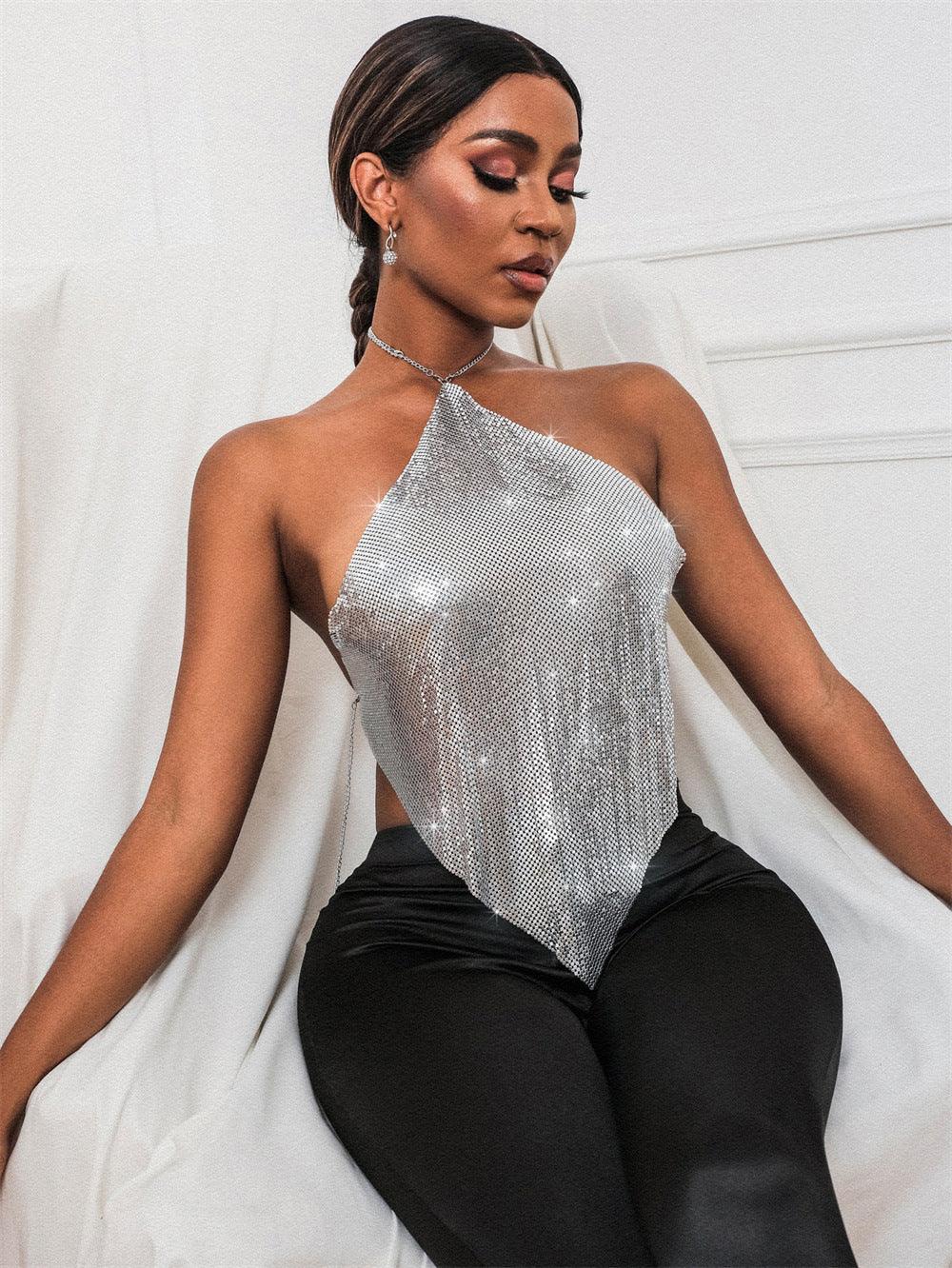 Woman posing indoors wearing a silver sequin halter top and black pants, with braided hair and earrings