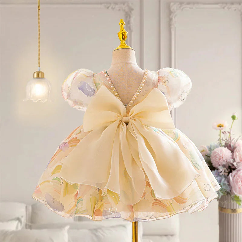 Baby girl's pastel floral dress with puff sleeves and large cream bow on mannequin in elegant room