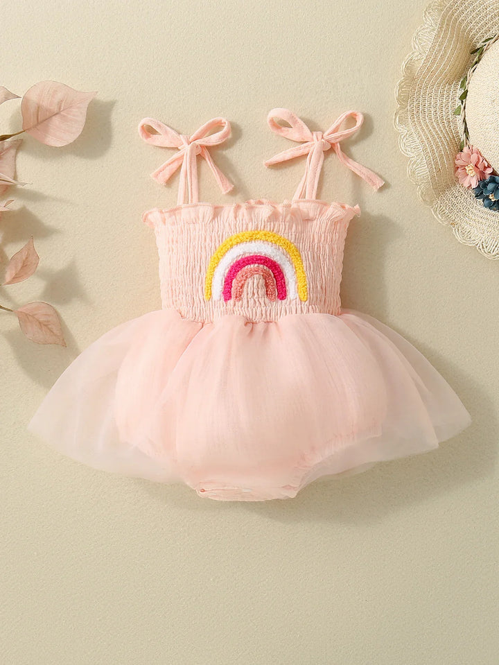 Pink baby romper with smocked bodice, rainbow embroidery, and tulle skirt on beige background