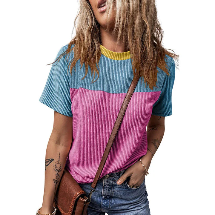 Woman wearing colorblock blue and pink textured short sleeve top with yellow collar and brown crossbody bag