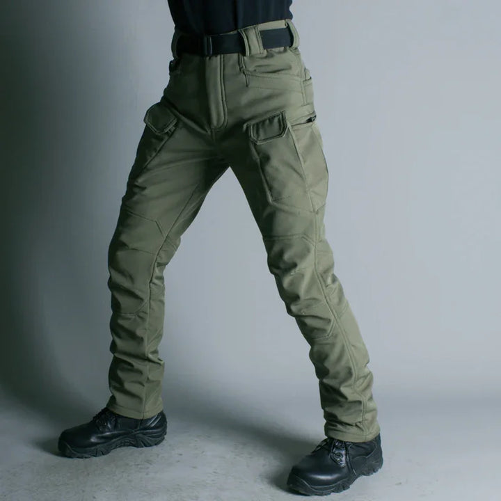 Person wearing olive green tactical cargo pants with side pockets and black boots against gray background