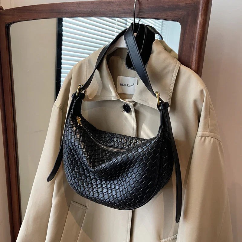 Black woven leather shoulder bag hanging on beige trench coat on wooden hanger
