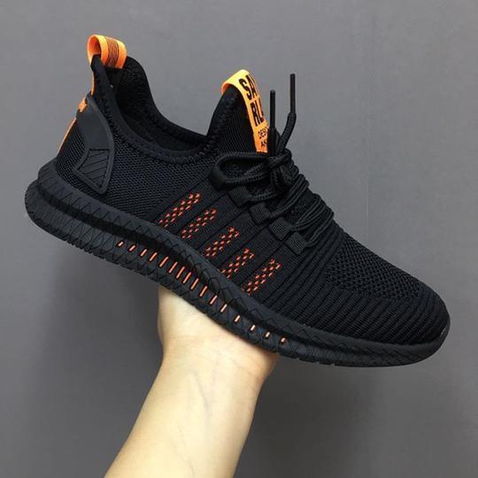 Black athletic sneaker with orange accents and knitted mesh upper held against gray background