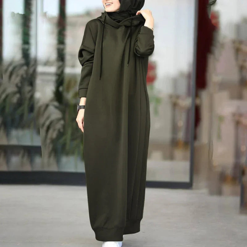 Woman wearing olive green long hooded abaya dress with black hijab and white shoes outdoors