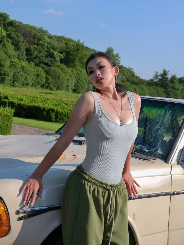 Young woman in white tank top and green pants posing by vintage car with broken windshield outdoors