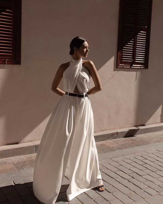 Woman in elegant white halter-neck dress with black belt standing on cobblestone street in sunlight