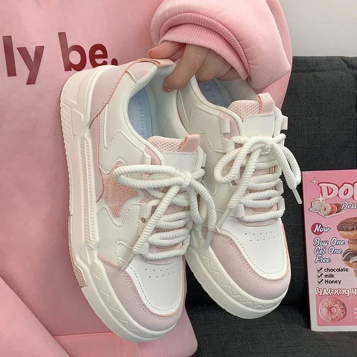 Hand holding white and pink star design chunky sneakers with thick white laces, beside pink donut promo flyer