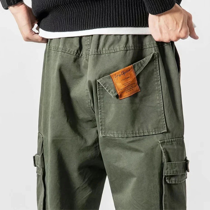 Close-up of olive green cargo pants with back and side pockets and a brown label on back pocket