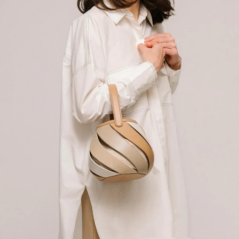 Woman in white oversized shirt holding a beige and tan spiral leather handbag
