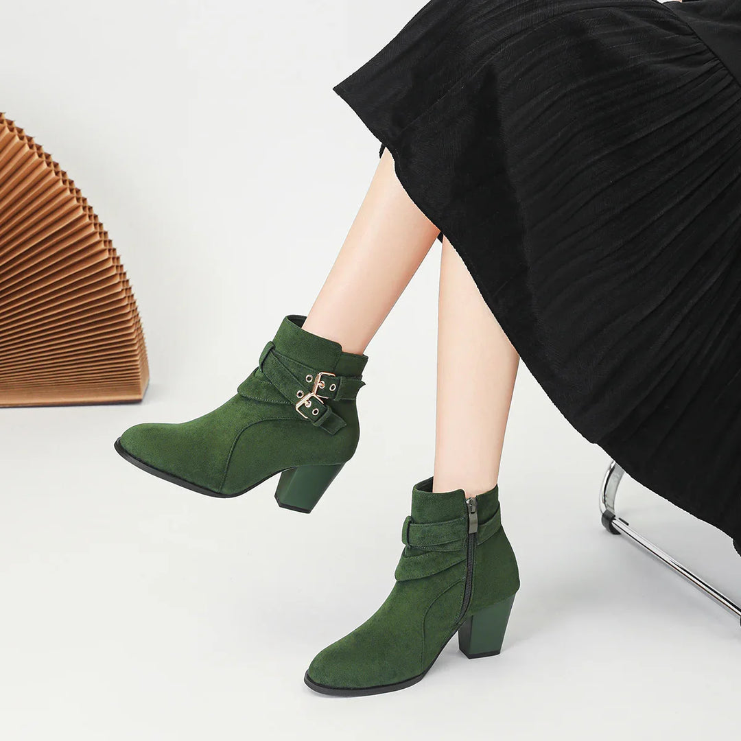 Woman wearing green suede ankle boots with block heels and buckle straps, paired with a black pleated skirt