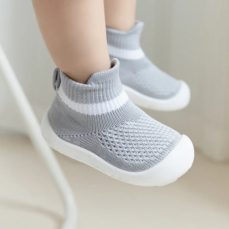 Baby feet wearing grey knit sock shoes with white soles and a white stripe detail