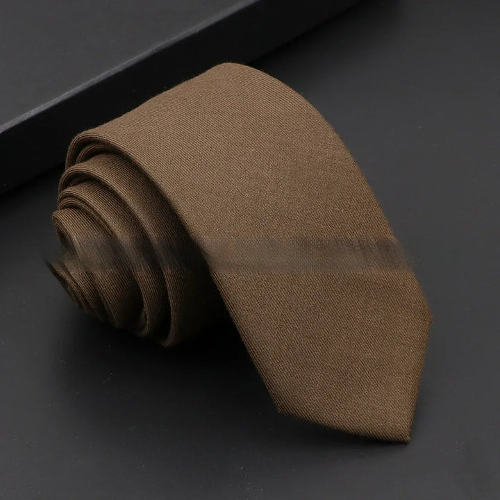 Rolled brown solid silk necktie on black surface with dark background