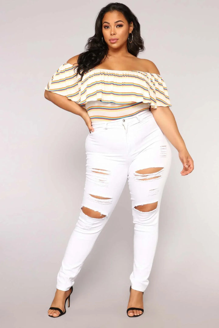 Curvy woman in off-shoulder striped top and white ripped skinny jeans with black heels