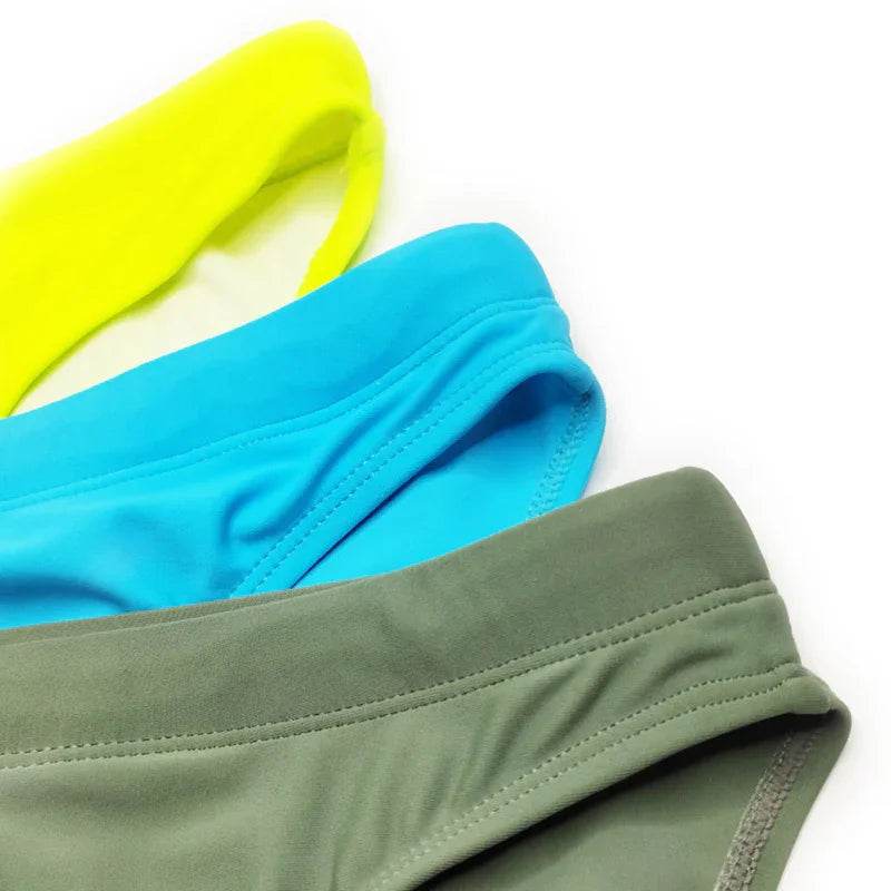 Close-up of colorful swim briefs in yellow, blue, and olive green on white background
