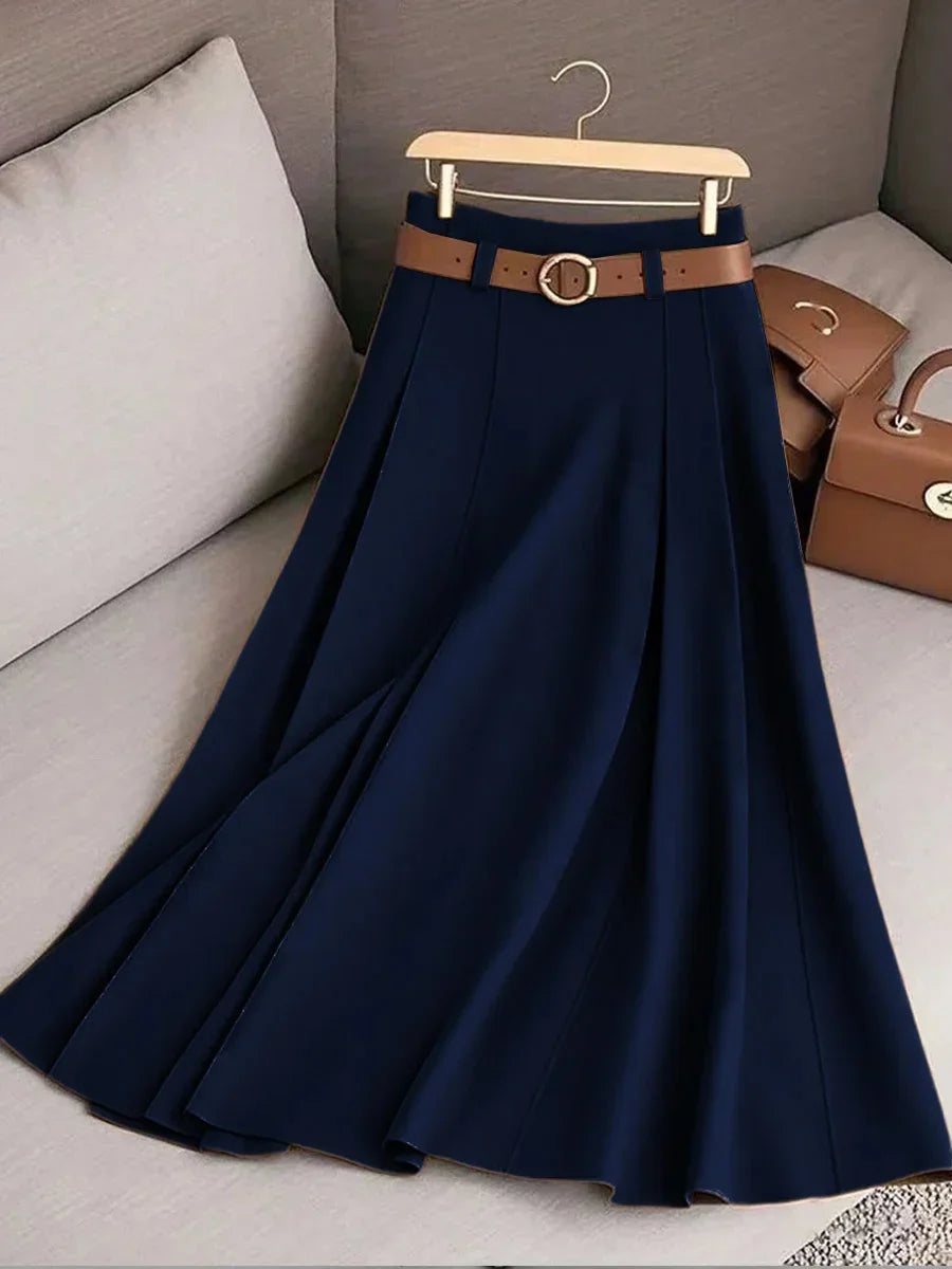 Navy blue pleated skirt with brown belt on wooden hanger, on beige sofa with matching brown bags