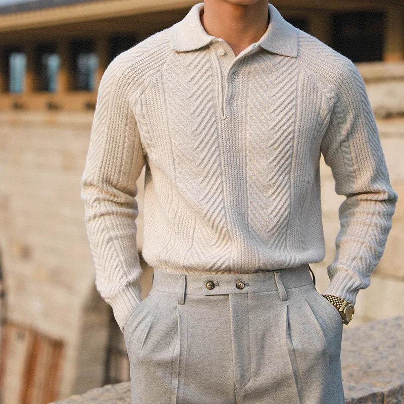 Man wearing beige cable knit polo sweater paired with light grey pleated trousers outdoors