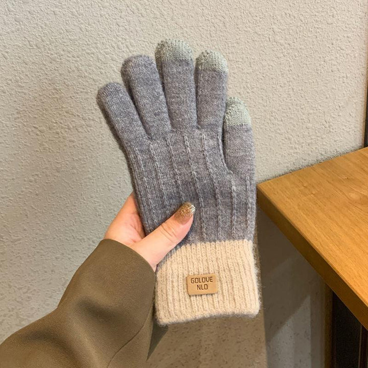 Hand holding gray knit gloves with white cuffs and label, textured wall and wooden table background