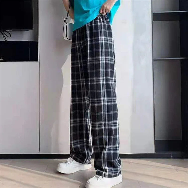 Person wearing black and white plaid wide-leg pants and white sneakers standing indoors