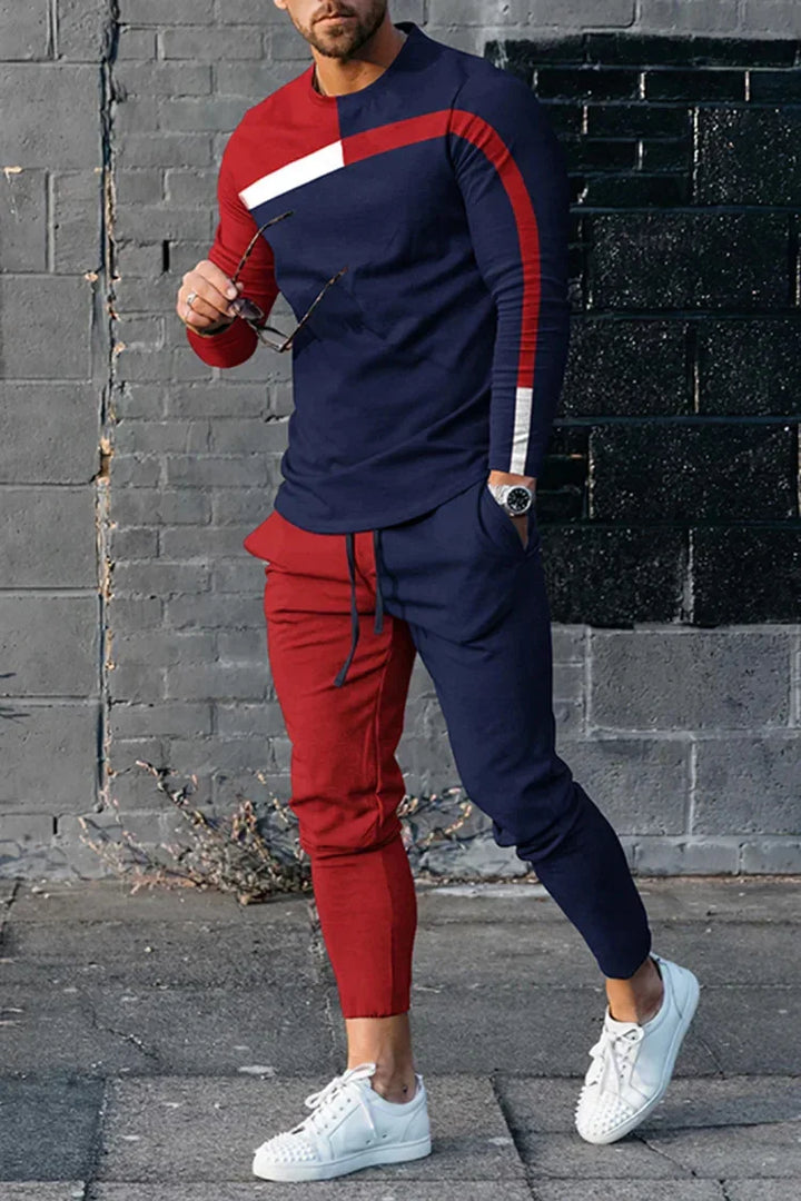 Man wearing color block red and navy blue casual tracksuit with white sneakers, standing by brick wall