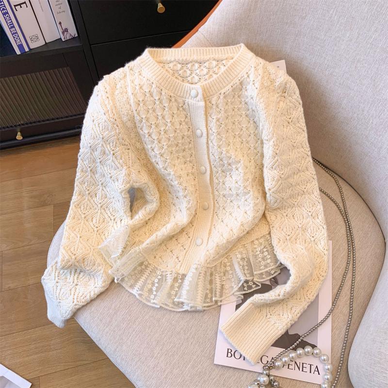 Cream-colored knitted cardigan with intricate lace details and pearl button closure on a beige chair