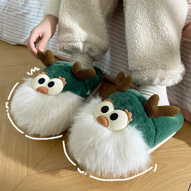 Cozy green plush reindeer slippers with large eyes, brown antlers, and fluffy white beards on wooden floor