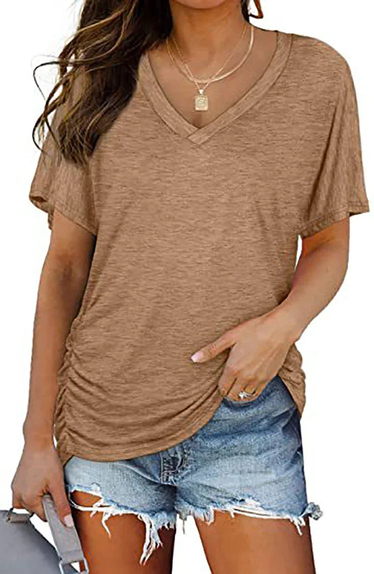 Woman wearing brown V-neck casual top with ruching and ripped denim shorts holding gray bag