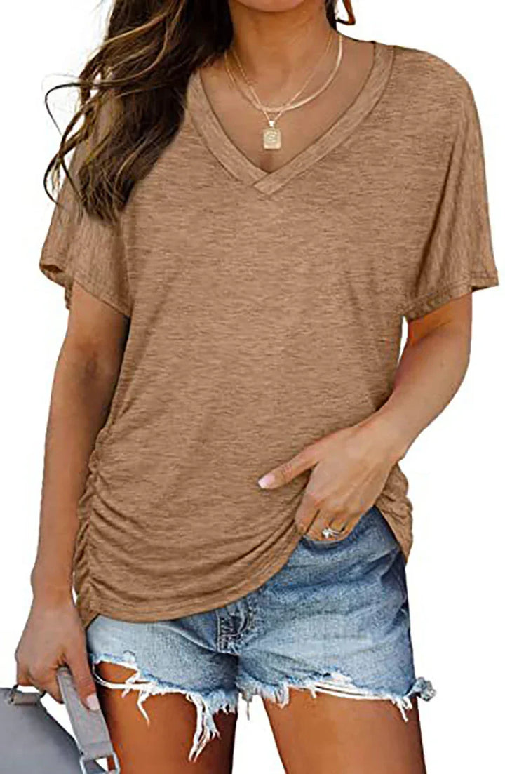 Woman wearing brown V-neck casual top with ruching and ripped denim shorts holding gray bag