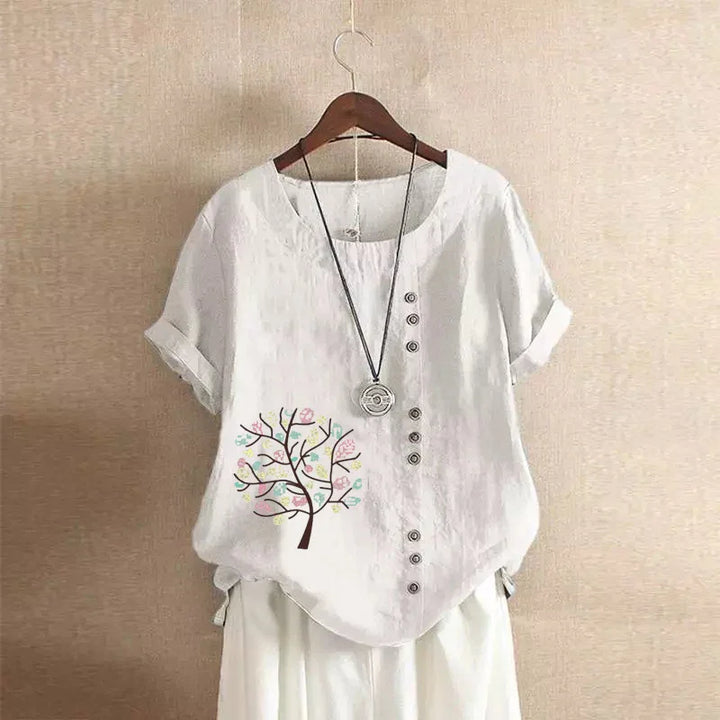 White short-sleeve linen blouse with button details and colorful tree print on left side
