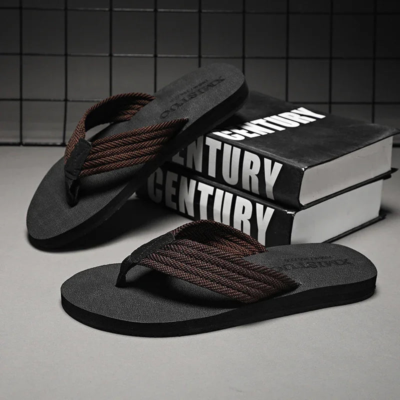 Black flip flops with brown braided straps placed on gray surface beside black books titled Century
