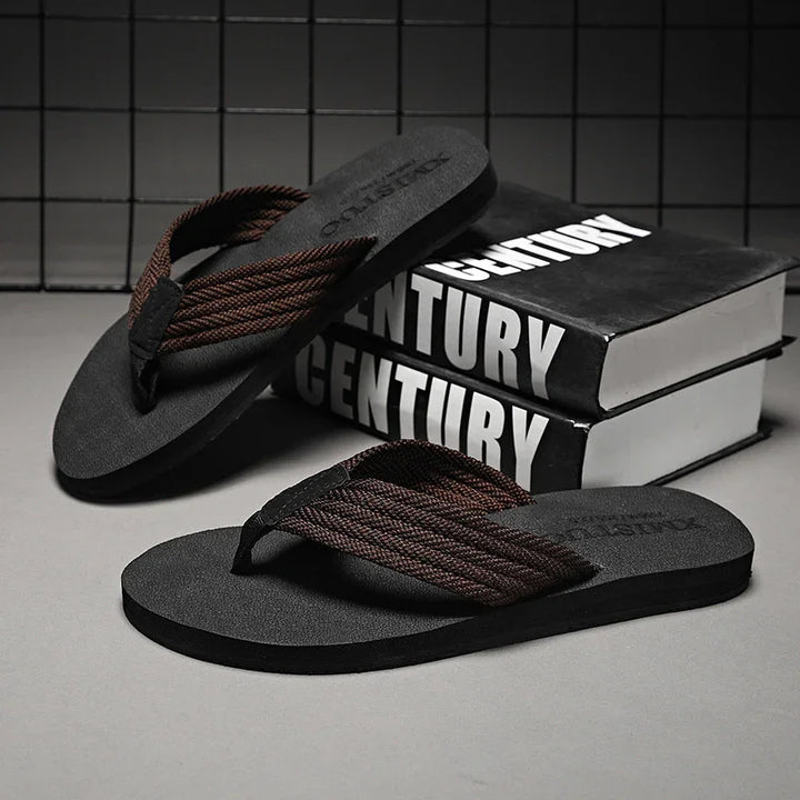 Black flip flops with brown braided straps placed on gray surface beside black books titled Century