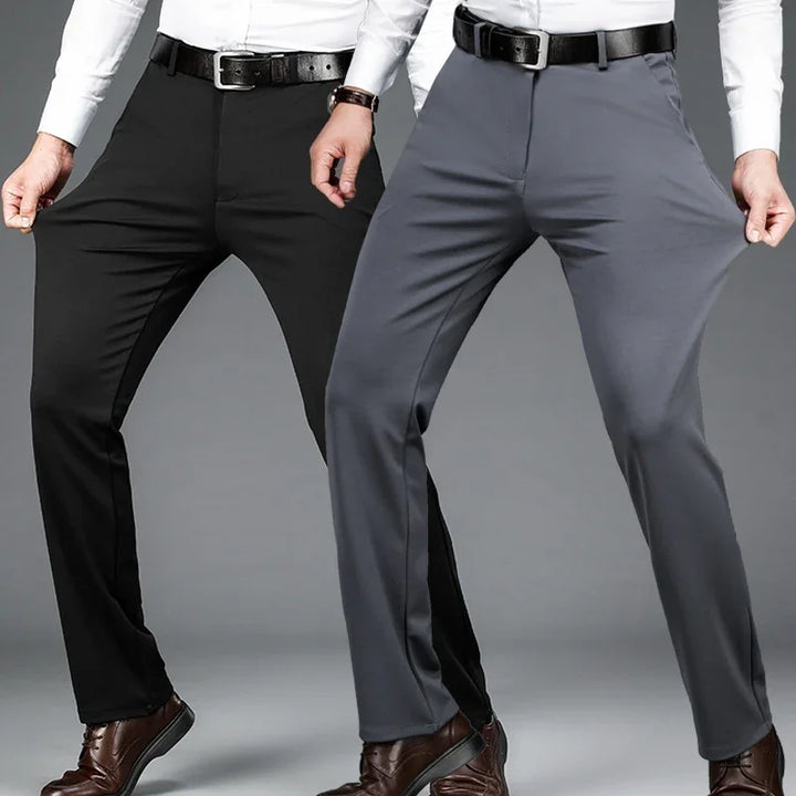 Men wearing stretchy black and gray dress pants with black belts and brown shoes against gray background