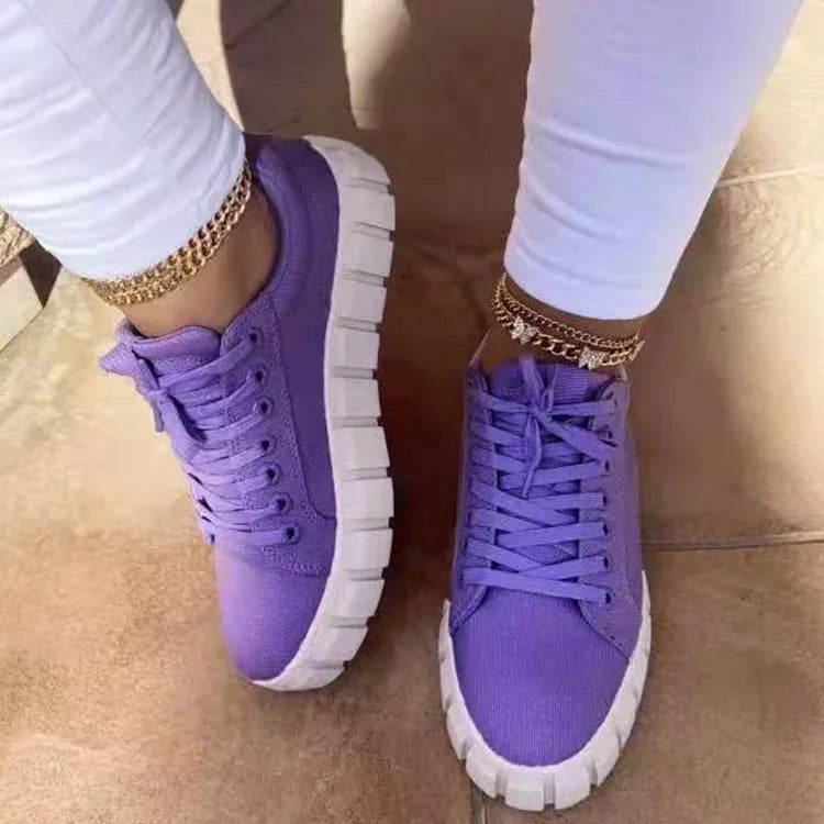 Close-up of feet wearing purple canvas sneakers with thick white soles and gold anklets on tiled floor