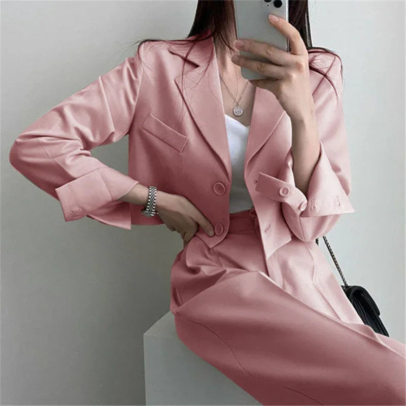 Woman taking a mirror selfie wearing a pink cropped blazer and high-waisted skirt with silver watch and necklace