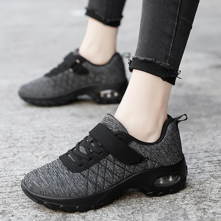Close-up of feet wearing stylish black and gray mesh sneakers with air cushion soles on textured ground