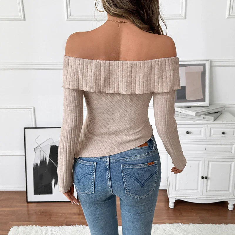 Woman wearing beige off-shoulder ribbed sweater and blue jeans in modern white room