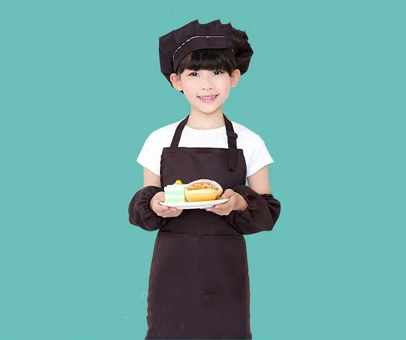 Smiling child chef in black apron and hat holding a plate with cake and sandwich on teal background