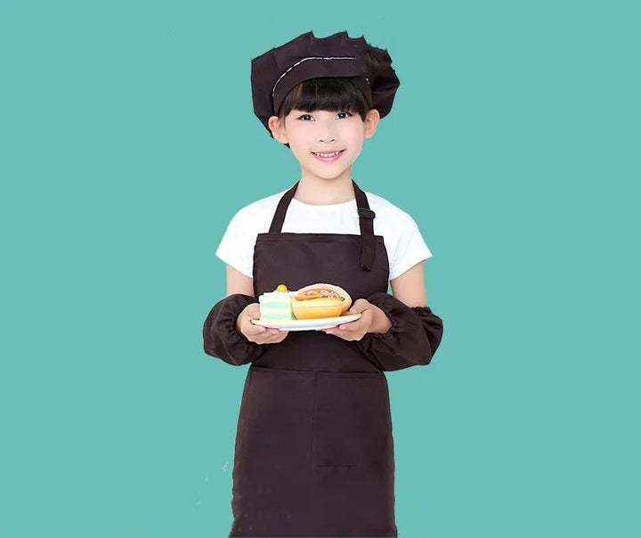 Smiling child chef in black apron and hat holding a plate with cake and sandwich on teal background