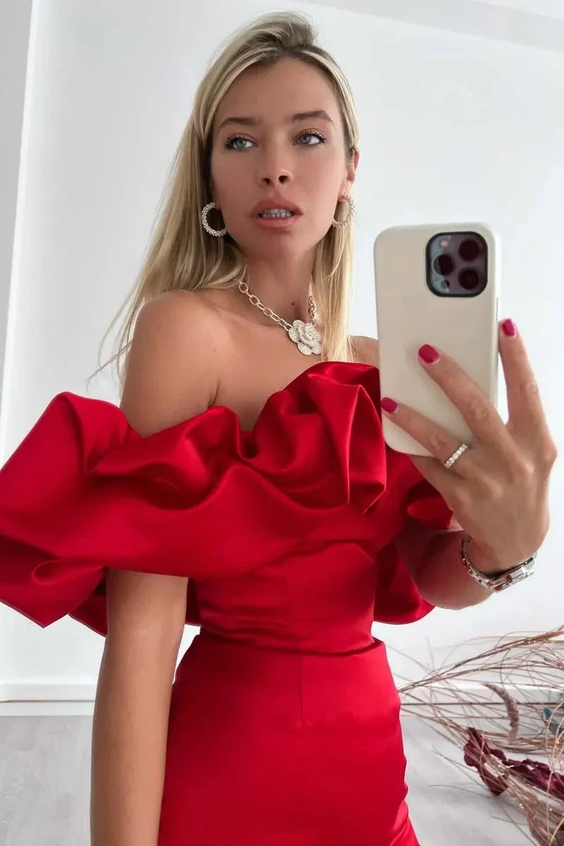 Blonde woman taking mirror selfie wearing off-shoulder red satin dress with ruffles and silver jewelry