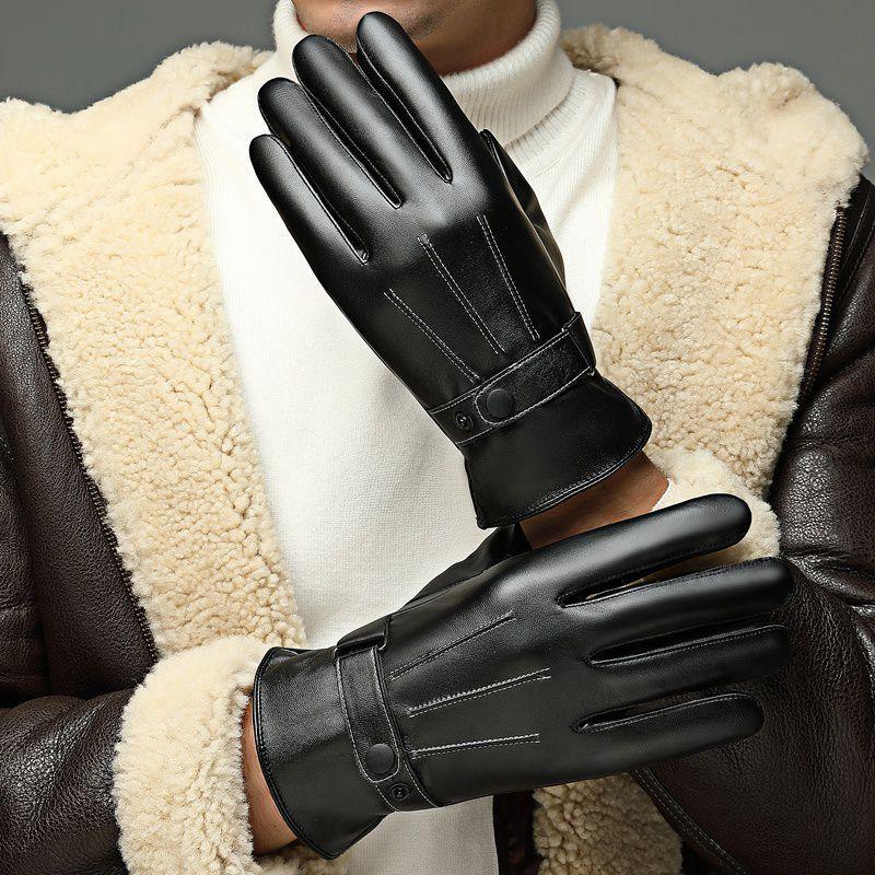 Person wearing black leather gloves with decorative stitching and button straps, paired with brown shearling jacket and white turtleneck