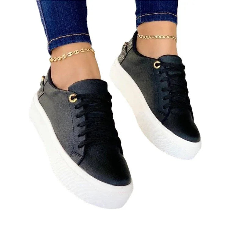 Black leather platform sneakers with white soles worn with blue jeans and gold anklets